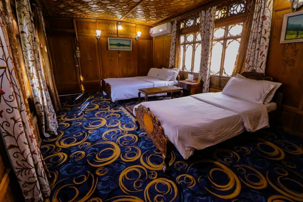 Duas camas em um quarto com janela e tapete azul.