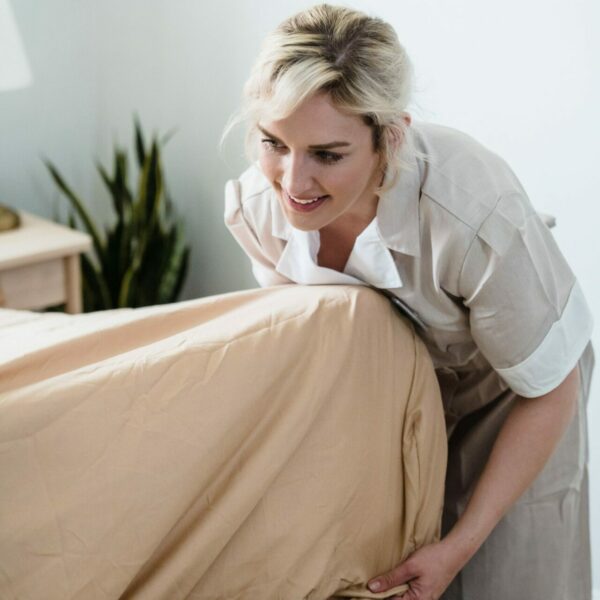 Mulher loira colocando roupa de cama em colchão.